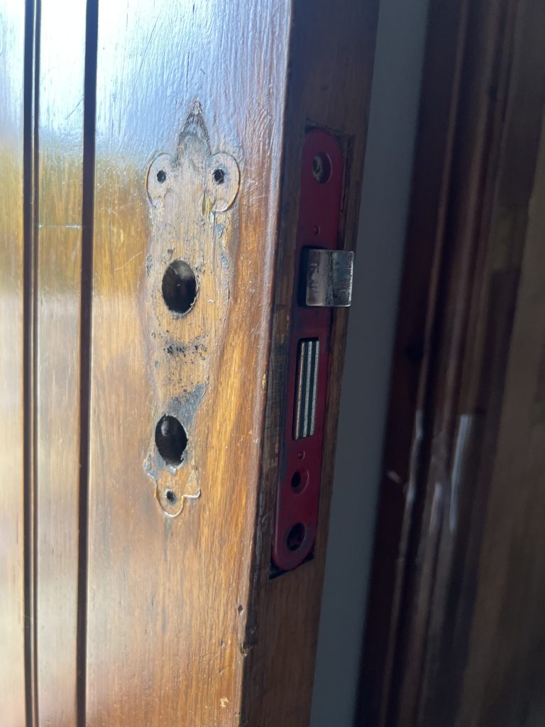 Closup of a wooden door with handle removed and mortice lock being changed.